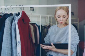 Retail employee checking inventory on a tablet in a small clothing store.