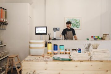 Small retail shop owner standing behind the counter using a tablet to manage orders and inventory.