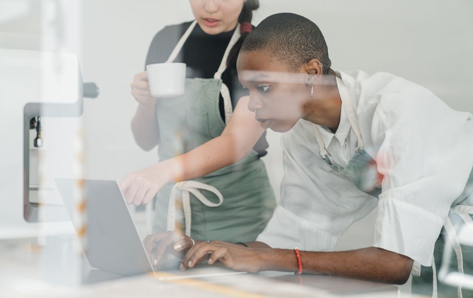 Two cafe staff using a laptop to manage bookings and online orders in a small restaurant.