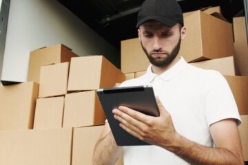 Local business owner using a tablet to check inventory inside a delivery van with stacked boxes.