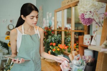Retail shop owner using a tablet to check orders and manage inventory in a small floral shop.