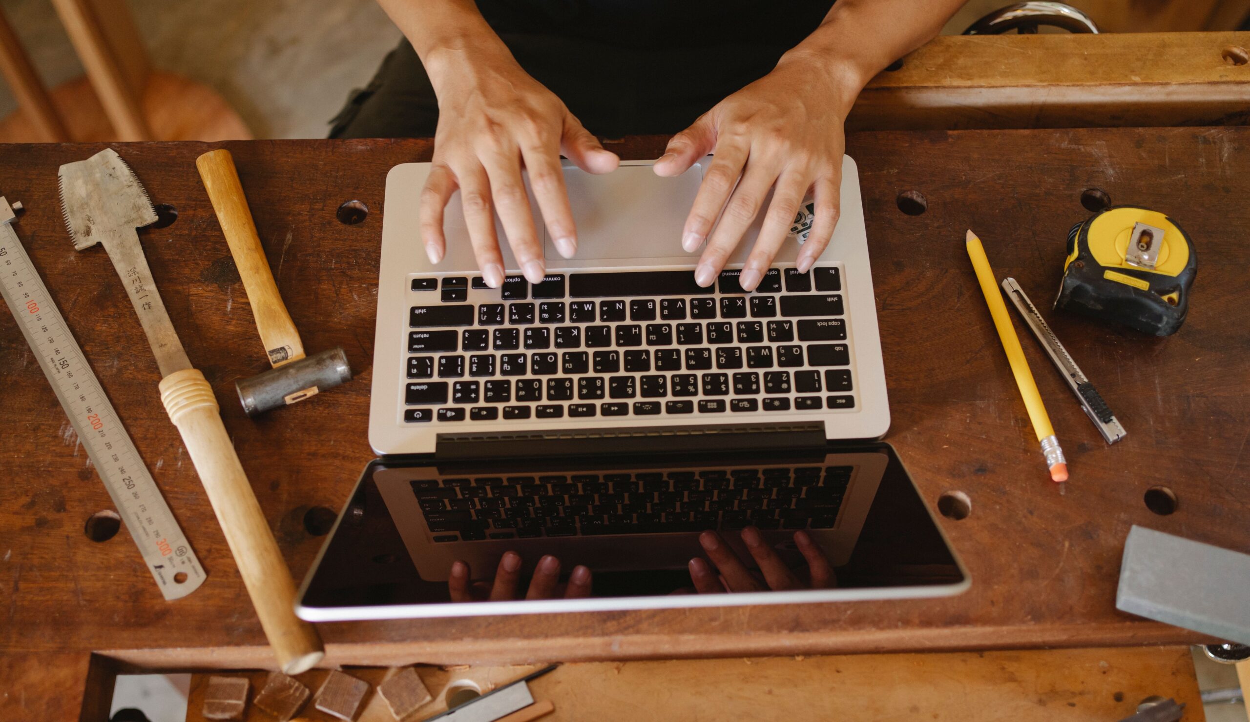 Workshop owner using a laptop at a wooden workbench in a carpentry workshop.