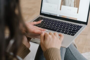 Local small business owner reviewing an e-commerce website on a laptop while seated in a shop-like setting.