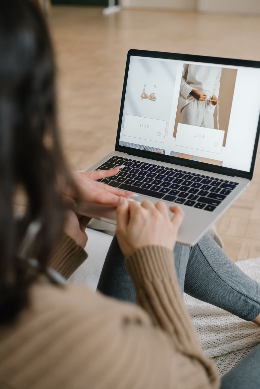 Local small business owner reviewing an e-commerce website on a laptop while seated in a shop-like setting.