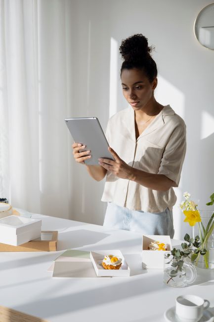 Small bakery owner using a tablet to manage orders and inventory in a bright kitchen shop.