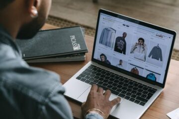 Small business owner reviewing online orders on a laptop inside a shop workspace.