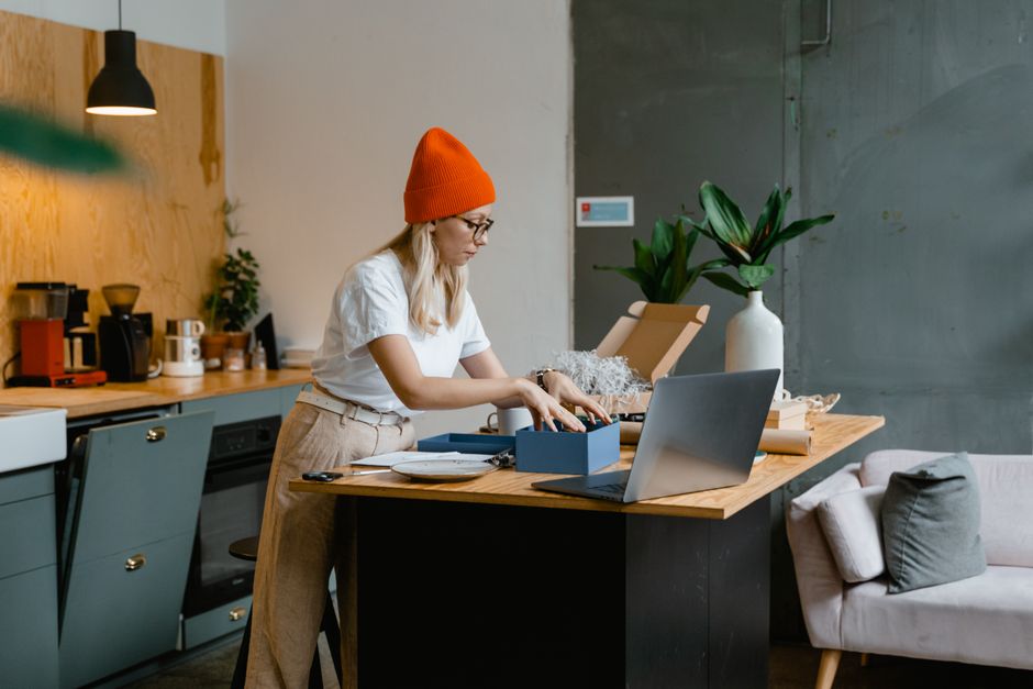 Small ecommerce owner unpacking and checking online orders with a laptop in a kitchen workspace.