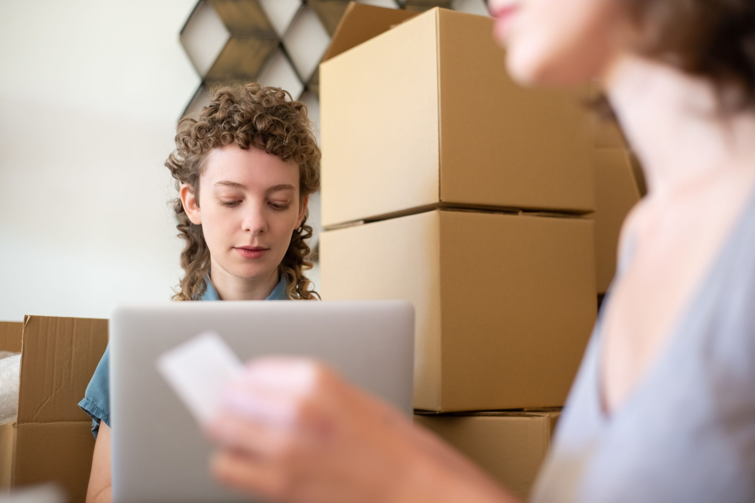 Two small business workers packing online orders with a laptop and cardboard boxes.